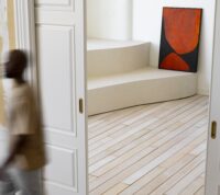foto desfocada de um homem a sair de uma sale, entre portas brancas com um quadro de arte contemporânea ao fundo